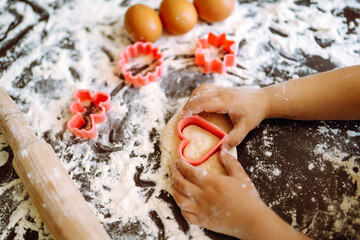 Fototapeta na wymiar A little chef cutting out shapes heart and making ginger cookies. Close up of boy hands carving dough. Easter baking preparation. Children's art project, a craft for children.