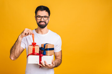 Wonderful gifts! Adorable photo of attractive bearded man with beautiful smile holding birthday present boxes isolated over yellow background.