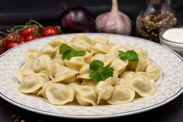 Russian small dumplings on a plate. Pelmeni. Black background.