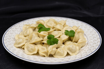 Russian small dumplings on a plate. Pelmeni. Black background.