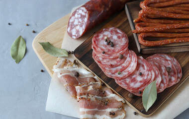 Slicing from different types of meat.Raw sausage , bacon, smoked sausages on wooden boards with bay leaves and black pepper on a gray background.