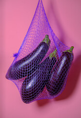 Eggplants in net bag. Pink background. Vegetables.