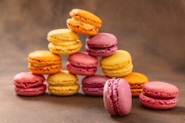 Macaroons. Multicolored Macaroons on a brown background. Pyramid. Pink, yellow and red Macaroons. French cake. Place for your text.