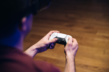 Closeup of man's hands playing video games on gaming console in front of TV widescreen. Man play...