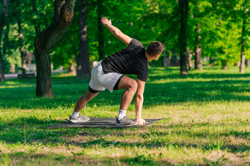 Attractive caucasian young man stretching and doing yoga exercises on the green grass in the park