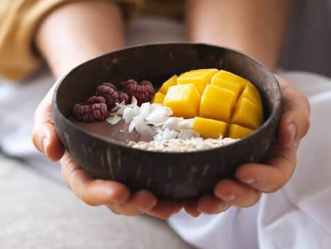 Crop anonymous female holding power bowl with fresh tasty mango and coconut chips in daytime