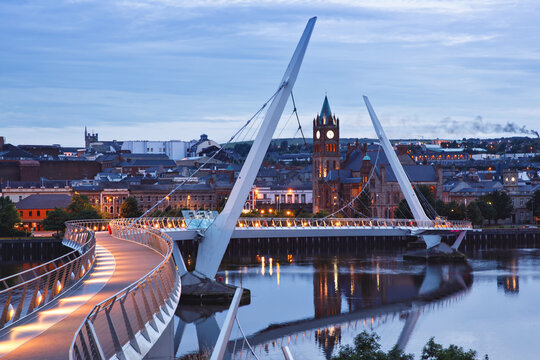 Derry, Ireland. Illuminated Peace bridge in Derry Londonderry, City of Culture, in Northern Ireland with city center at the background. Night cloudy sky with reflection in the river at the dusk