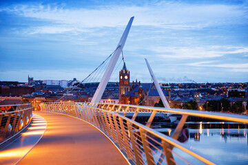 Derry, Ireland. Illuminated Peace bridge in Derry Londonderry, City of Culture, in Northern Ireland with city center at the background. Night cloudy sky with reflection in the river at the dusk