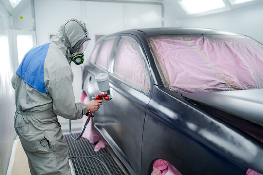 Side view of male in respiratory mask and protective suit painting car with spray gun in service
