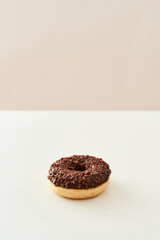 Dessert that will melt in your mouth. Vertical shot of a freshly baked delicious chocolate donut with sprinkles on white and beige background