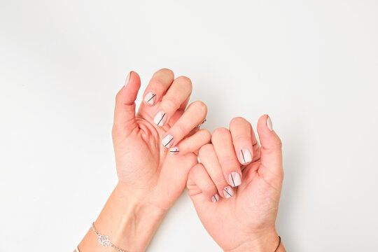 Top view of crop anonymous female demonstrating hands with stylish elegant manicure with geometric pattern and black lines on white background