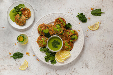 Top view yummy appetizing herbal fritters garnished with healthy green sauce parsley and lemon slices on white table