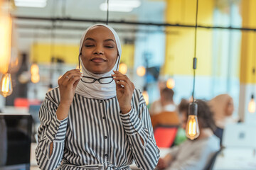 Protrait of a black ( african-american) female muslim standing in a modern business office while wearing a hijab.