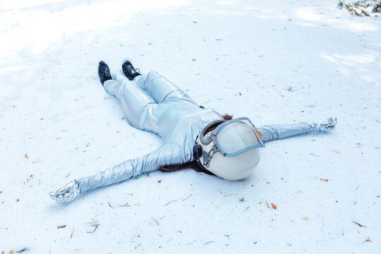 Full body fit calm spacewoman in costume and helmet lying with arms outstretched on snowy glade in winter forest