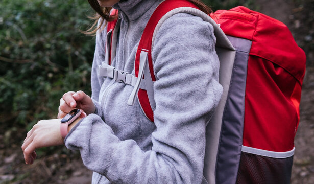 Side view of crop female in activewear with backpack using GPS on fitness tracker for navigation during hiking in forest