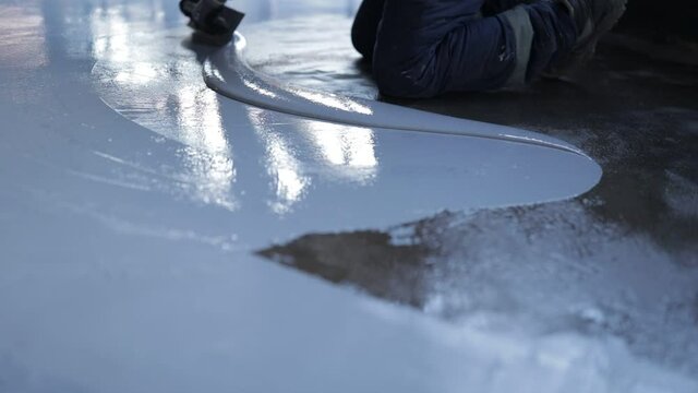 Worker, coating floor with self-leveling epoxy resin in the workshop of the plant