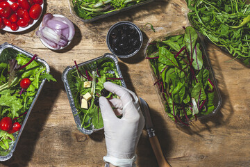 Top view crop anonymous chef in glove adding black olives to mix leaves salad with butter cubes