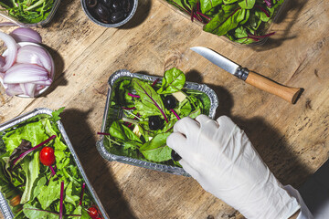 Top view crop anonymous chef in glove adding black olives to mix leaves salad with butter cubes