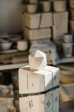 Light studio with ceramic three dimensional geometric figures on surface near shelf with handmade clayware