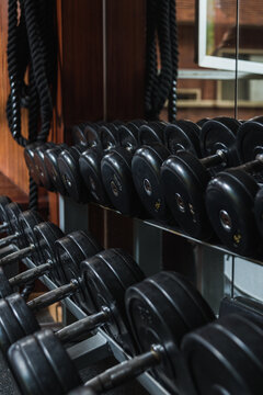 Heavy black dumbbells with metal bars and plates reflecting in mirror in gymnasium in daytime