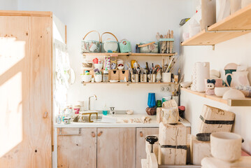 Studio with wooden shelves with different instruments for pottery and utensil near sink in daylight
