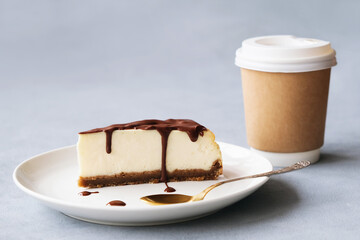 Slice of cheesecake poured chocolate sauce on plate and disposable coffee container. Sweet delicious and hot drink. Coffee time concept.