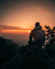 Hiker with backpack standing on top of a mountain and enjoying sunrise.