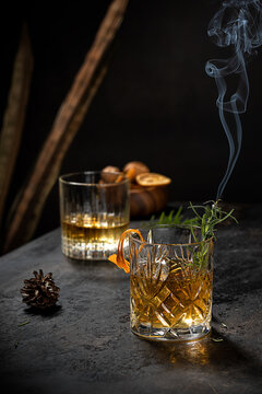 Crystal glass of old fashioned whiskey drink garnished with fresh rosemary and orange peel on black table