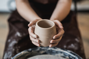 Fototapeta na wymiar Hands of a potter, creating an earthen jar on the circle