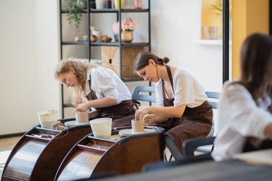 Young women learning to sculpt with a clay on a pottery wheel during a lesson at workshop in art studio.