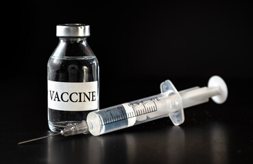 Glass vaccine vial on black board, hypodermic syringe near
