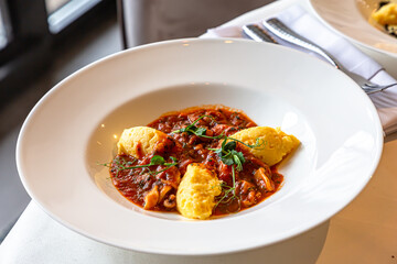 Polenta with seafood in tomato sauce is on a plate on the table in a restaurant
