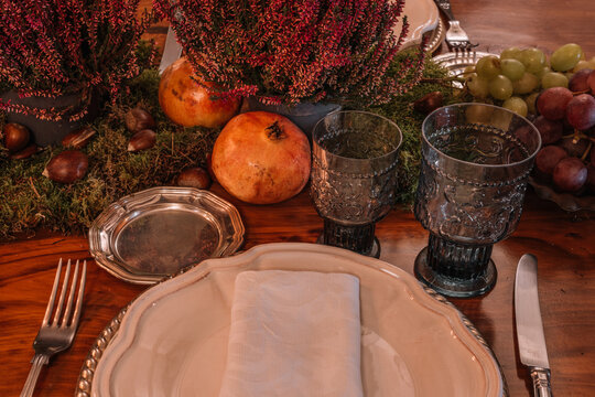 High angle of crystal glasses near plate and cutlery placed on table decorated with grapes Calluna vulgaris flowers and pomegranate