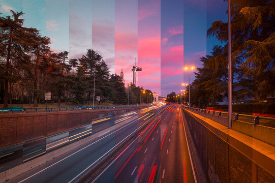 Asphalt roadways with driving vehicles between high trees under bright cloudy sky in town at sundown