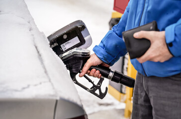 Man holding fuel nozzle, filling gas tank of diesel car covered with snow