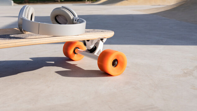 Contemporary wireless headset on longboard with bright wheels in skate park on sunny day