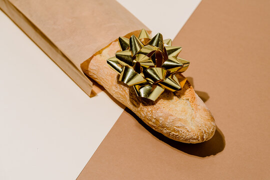 Minimalistic still life composition with fresh artisan bread loaf in paper package with golden gift bow on table