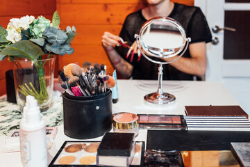 Crop unrecognizable transsexual man at table with collection of beauty products and mirror in cabin
