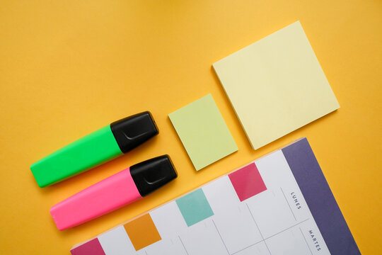 Top view flat lay composition with colorful markers and sticky notes arranged near planner calendar on yellow background