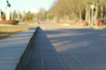 Spring in the city, the sunlit empty street paved with stone next to the park. Close-up view from sidewalk level