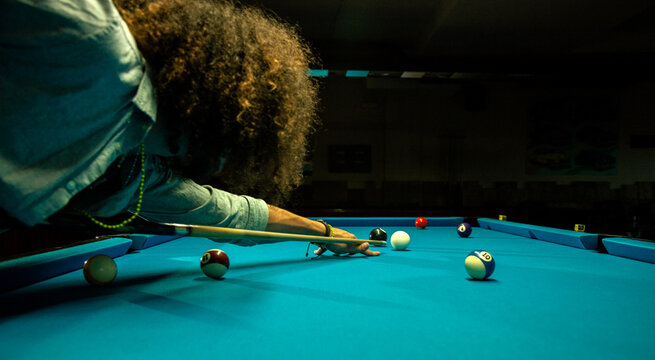 Crop focused bearded male hitting ball with cue while playing game in billiard pool