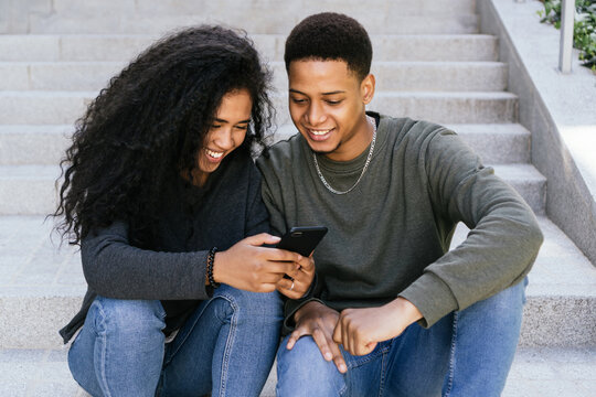 Happy black couple surfing together with smartphone in the city. Afro American couple communicating online via internet. Afro man and woman in a virtual meeting on the street.