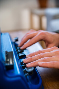Crop anonymous visually impaired male typing on typewriter with tactile writing system at home
