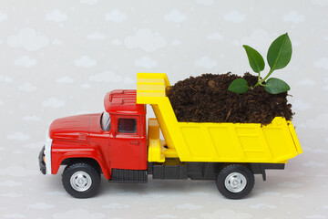 Toy dump truck delivering fertile soil with a young sprout