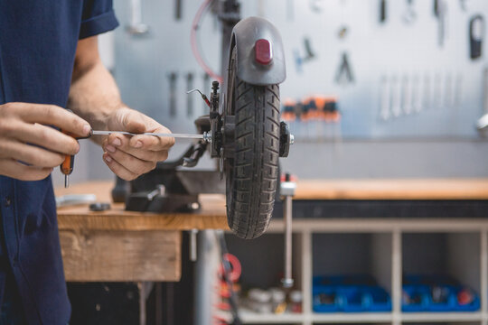 Side view of crop anonymous male mechanic with screwdriver fixing wheel of electric scooter in workshop