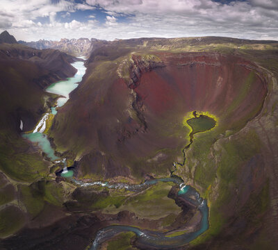 Amazing view of curvy blue river loop streaming on rough hilly terrain covered with lush abundant vegetation in Iceland