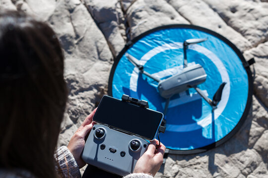 From above of unrecognizable female with remote controller standing on beach with drone placed on landing pad