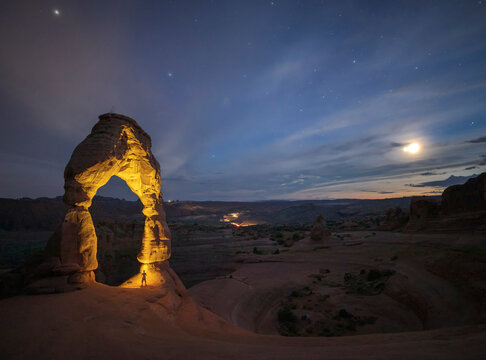 Amazing landscape with arched formation in red rock near rare vegetation located in national park against cloudy sky in USA