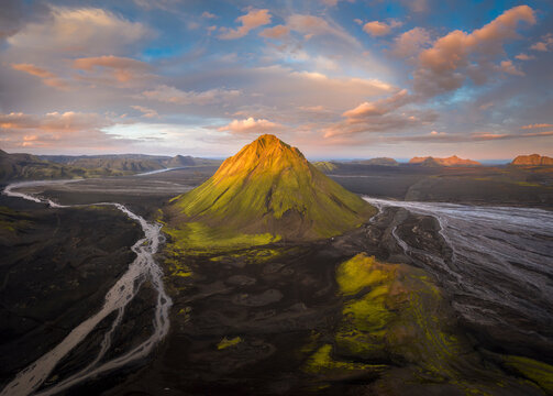 Establishing shot of vast valley covered with grass and many narrow curvy rivers near rough desolated hills against blue sky in Iceland
