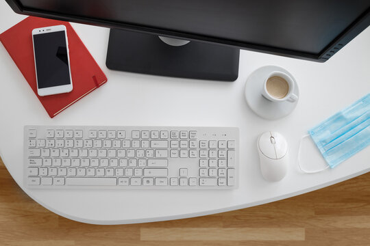 Modern Computer And Smartphone With Notebook Placed On White Table With Medical Mask In Light Office